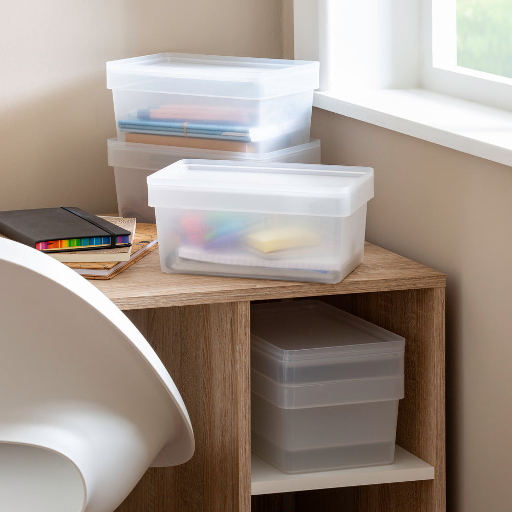 Clear storage boxes on a wooden shelf next to a chair with books and stationery.